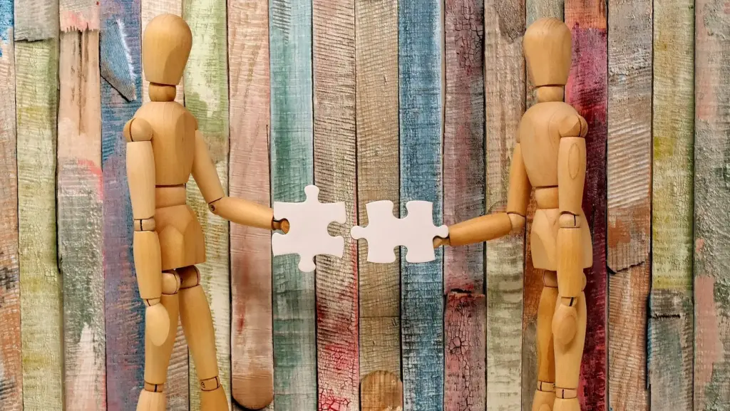 two wooden people models putting two pieces of a puzzle together