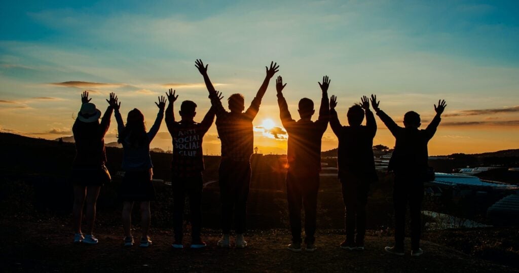 people holding up there hands watching the sun go down