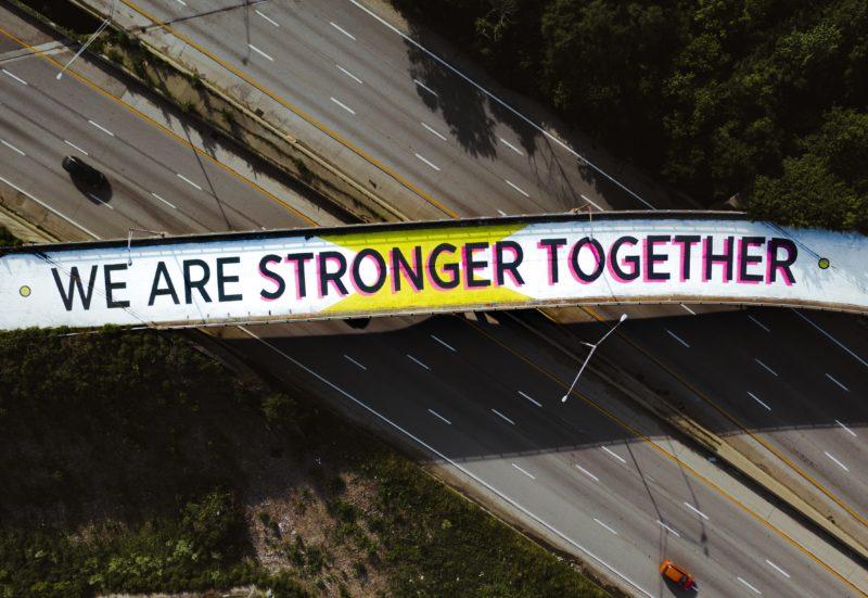 a walkway over a freeway painted to say we are stronger together