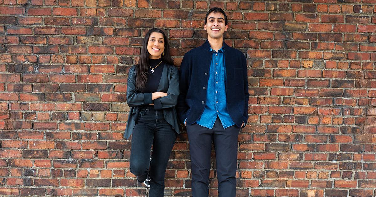 Sonia Nigam and Amar Shah standing together behind a brick wall