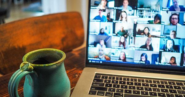 a mug of coffee next to a macbook on a video call