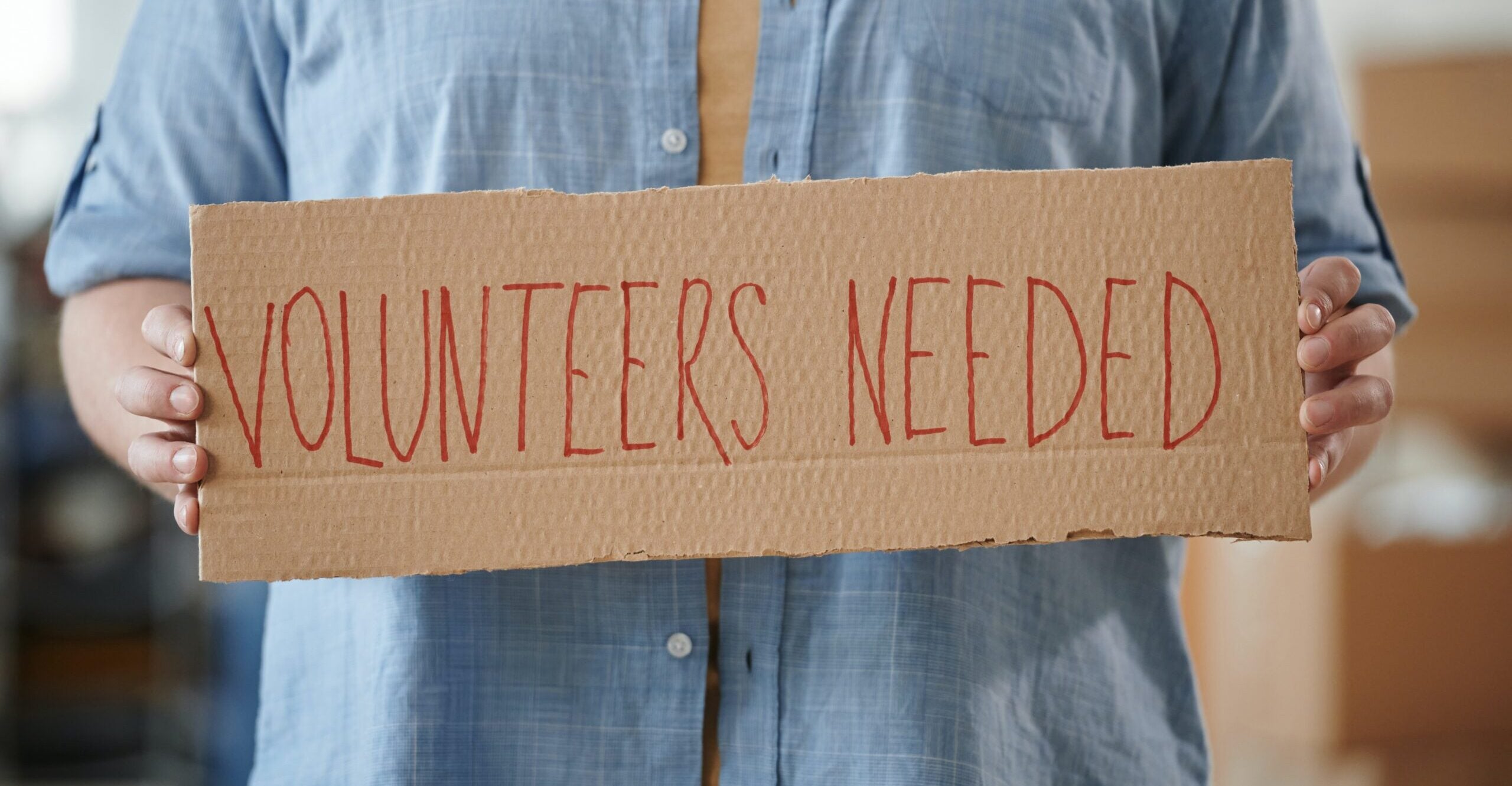 someone holding a sign that says Volunteers needed